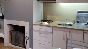 Cozinha com fogão a gás, pia e armários. Há uma lareira com proteção e uma cadeira.