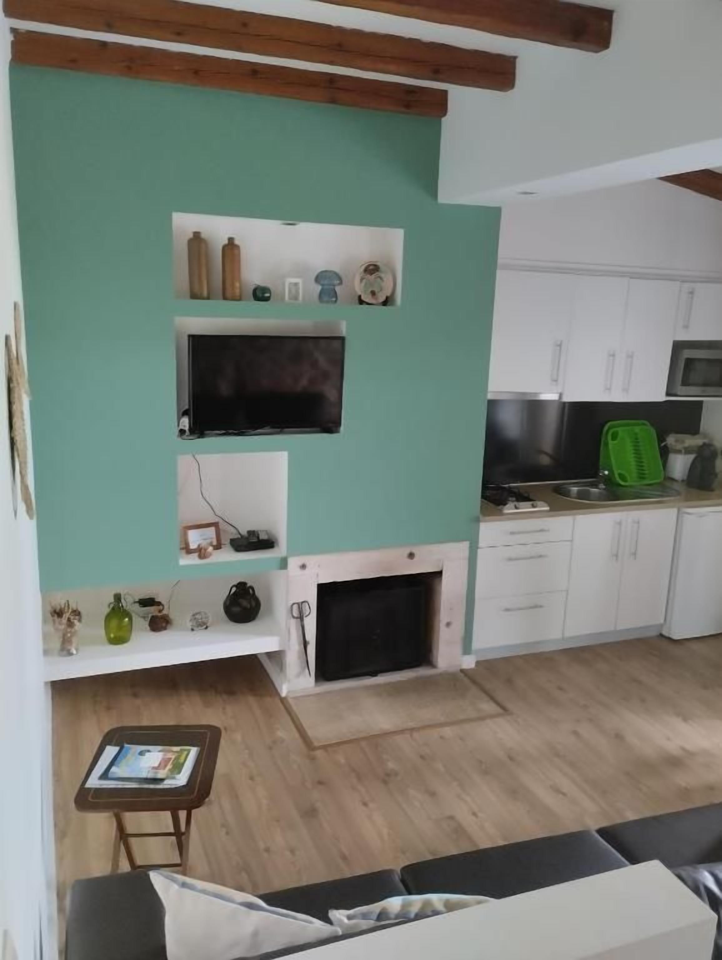 A living room with a fireplace, a television mounted on the wall, and a kitchen area with cabinets and appliances.