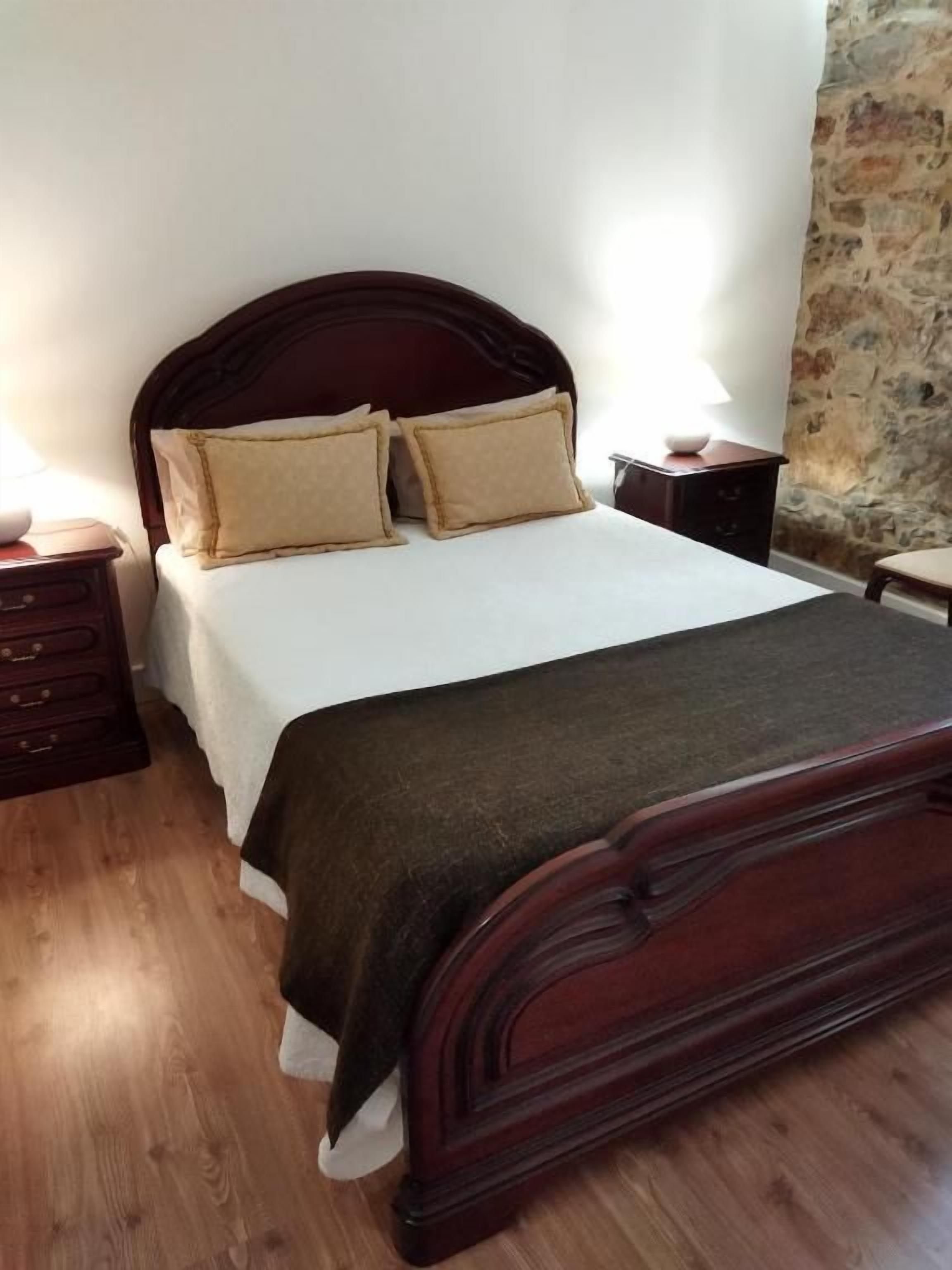 A bedroom with a wooden bed, a nightstand, and a stone wall.
