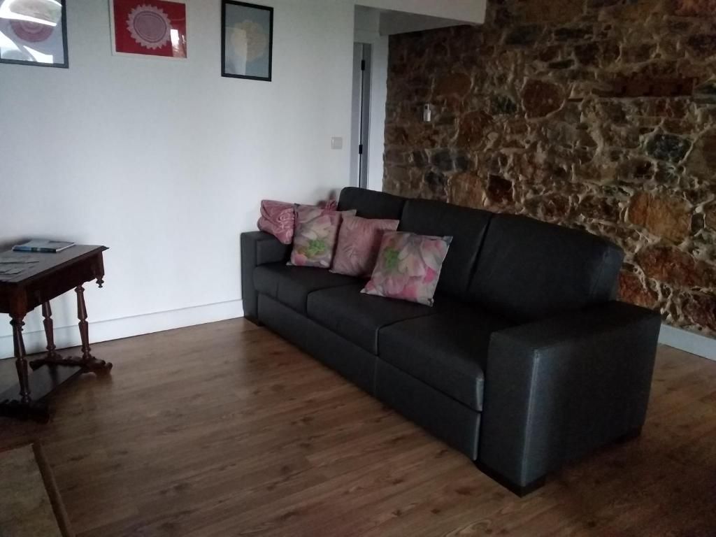 A living room with a black sofa, a wooden coffee table, and a stone wall.