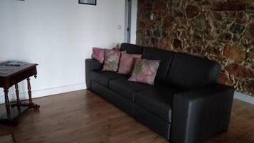 A living room with a black sofa, a wooden coffee table, and a stone wall.