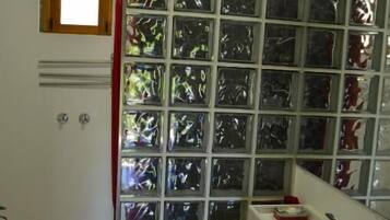 A bathroom with a glass shower enclosure, a white sink with a red basin, and a mirror above the sink.