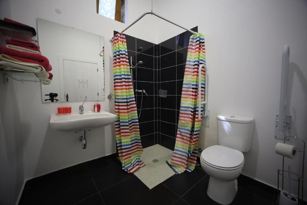 Un baño con ducha, inodoro, lavamanos y un perchero con toallas dobladas.