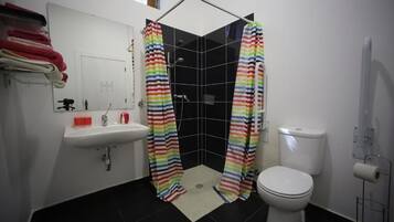 Un baño con ducha, inodoro, lavamanos y un perchero con toallas dobladas.