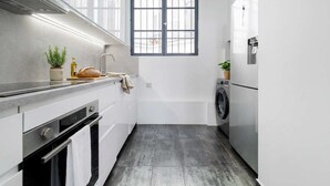 A compact kitchen with a built-in oven, a washing machine, and a window with bars. - FurtiveStay - Sentier - 5 Jeuneurs - 2BDR 6P (Paris)