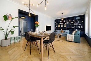 Ein modernes Wohnzimmer mit Essbereich, Bücherregal und einer großen Topfpflanze.