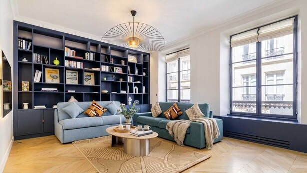 A living room with a sofa, coffee table, bookshelf, and large windows. - FurtiveStay - Sentier - 5 Jeuneurs - 2BDR 6P (Paris)