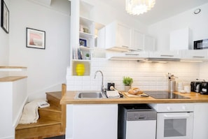 A modern kitchen with white cabinetry, a wooden countertop, a built-in dishwasher, and a microwave. - FurtiveStay - Champs Elysées - St Honoré - 3BDR 8P (Paris)