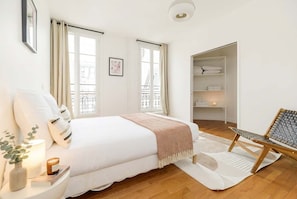 A bedroom with a bed, bedside table, lamp, and a chair. - FurtiveStay - Champs Elysées - St Honoré - 3BDR 8P (Paris)