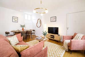 A living room with a sofa, armchair, TV, wooden cabinet, and a dining area with chairs and a table. - FurtiveStay - Champs Elysées - St Honoré - 3BDR 8P (Paris)