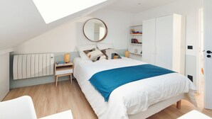 Ein Schlafzimmer mit Oberlicht, einem Bett mit blauer Decke, einem Nachttisch, einem Kleiderschrank und einer Heizung.