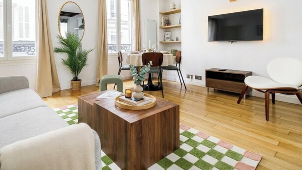 A modern living room with a sofa, a coffee table, a dining area with chairs, a TV mounted on the wall, and a plant. - FurtiveStay - Opéra - Hanovre - 1BDR 4P (Paris)