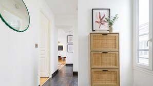 A hallway with a mirror, a wicker cabinet, and framed artwork. - FurtiveStay - Opéra - Hanovre - 1BDR 4P (Paris)