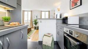A modern kitchen with grey cabinets, a microwave, an oven, and a small dining area with a checkered floor. - FurtiveStay - Opéra - Hanovre - 1BDR 4P (Paris)