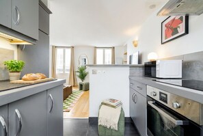 Eine moderne Küche mit grauen Schränken, einer Mikrowelle, einem Backofen und einer kleinen Essecke mit kariertem Boden.
