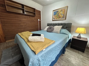 A bedroom with a bed, a nightstand, a lamp, a painting, and a wooden headboard. - Oceana Suites Refugio del Maipo (San José de Maipo)
