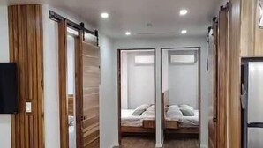 Ein Flur mit Holzboden, einem Bett mit weißem Kopfteil und einem Kühlschrank.