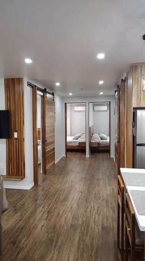 A hallway with a wooden floor, a bed with a white headboard, and a refrigerator. - Modern Nature Retreat Between Jungle & Ocean (Savegre)