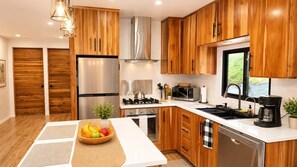 A modern kitchen with wooden cabinets, stainless steel appliances, and a central island with a fruit bowl. - Modern Nature Retreat Between Jungle & Ocean (Savegre)