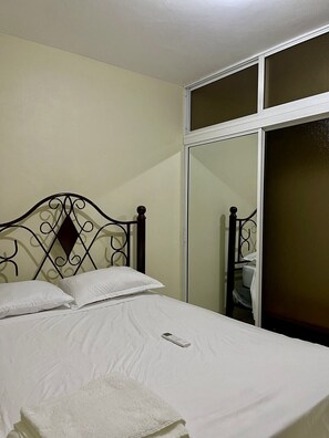 Una cama con cabecera de metal, almohada y manta blancos.