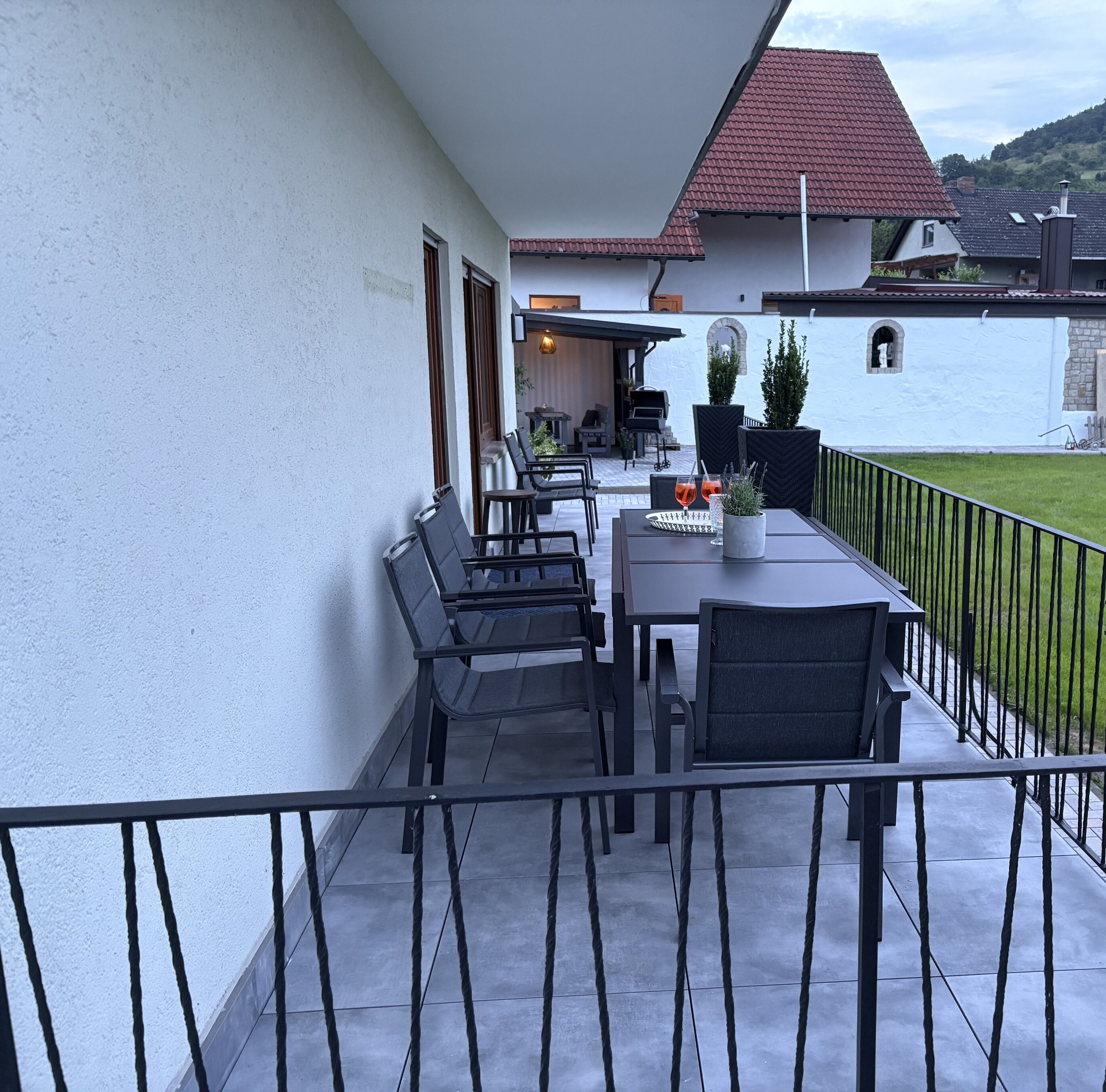 Eine Terrasse mit Tisch und Stühlen, einem Blumentopf und Blick auf ein Haus mit rotem Dach.