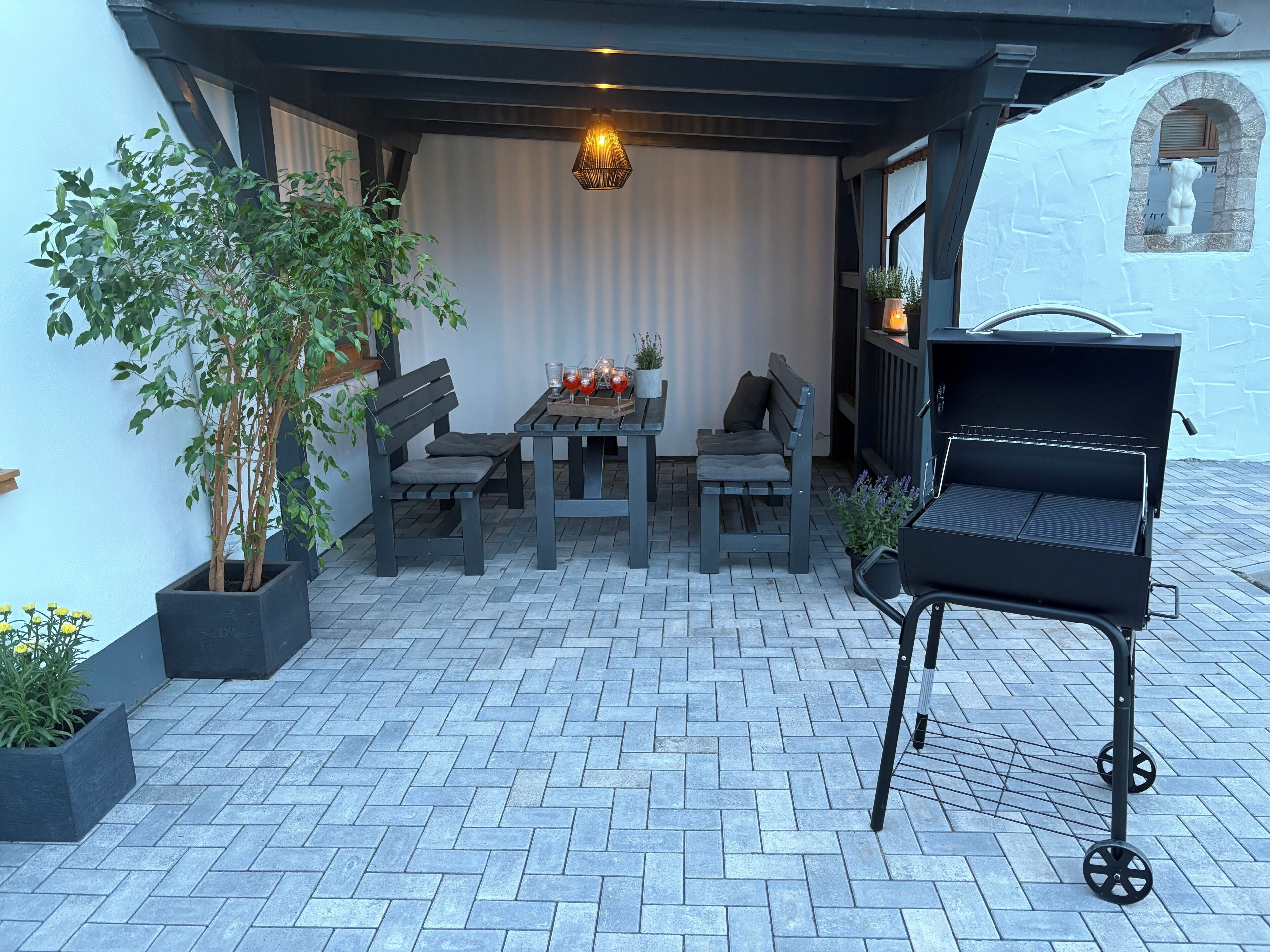 Een terras met een barbecue, twee tafels met stoelen en potplanten.