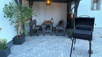 Een terras met een barbecue, twee tafels met stoelen en potplanten.