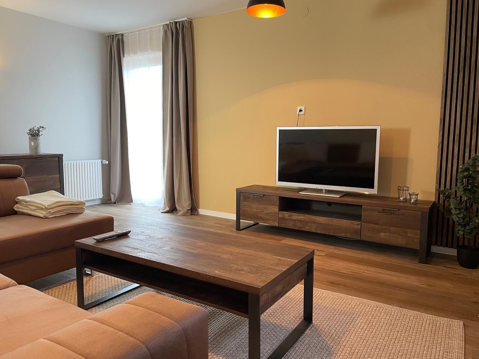 Ein modernes Wohnzimmer mit einer Couch, einem Couchtisch, einem Fernseher auf einem Holzgestell und einer Heizung.