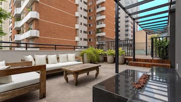 A rooftop patio with outdoor furniture, a grill, and a view of high-rise buildings.