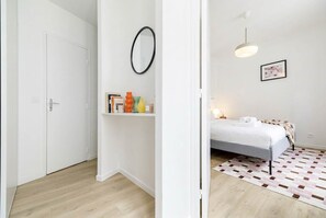 Ein Zimmer mit einem Bett, einem Nachttisch, einem Spiegel, einem Regal mit Büchern und Dekoration sowie einem gemusterten Teppich.