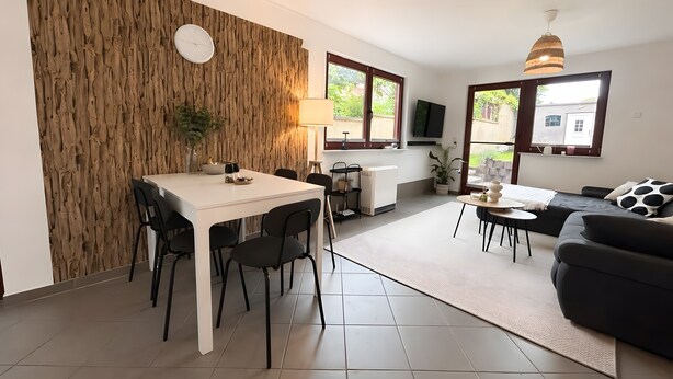 Un espace de vie moderne comprenant un coin repas, un canapé, un téléviseur et un mur d’accent en bois.