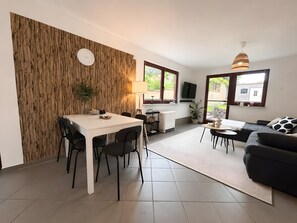 Ein moderner Wohnbereich mit Essplatz, einer Couch, einem Fernseher und einer Wand mit Holzverkleidung.