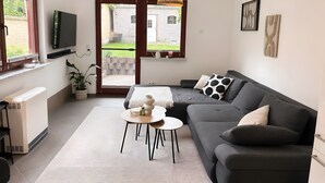 Un salon moderne avec un canapé, une table basse, un téléviseur et une vue sur l’extérieur grâce à une porte vitrée.
