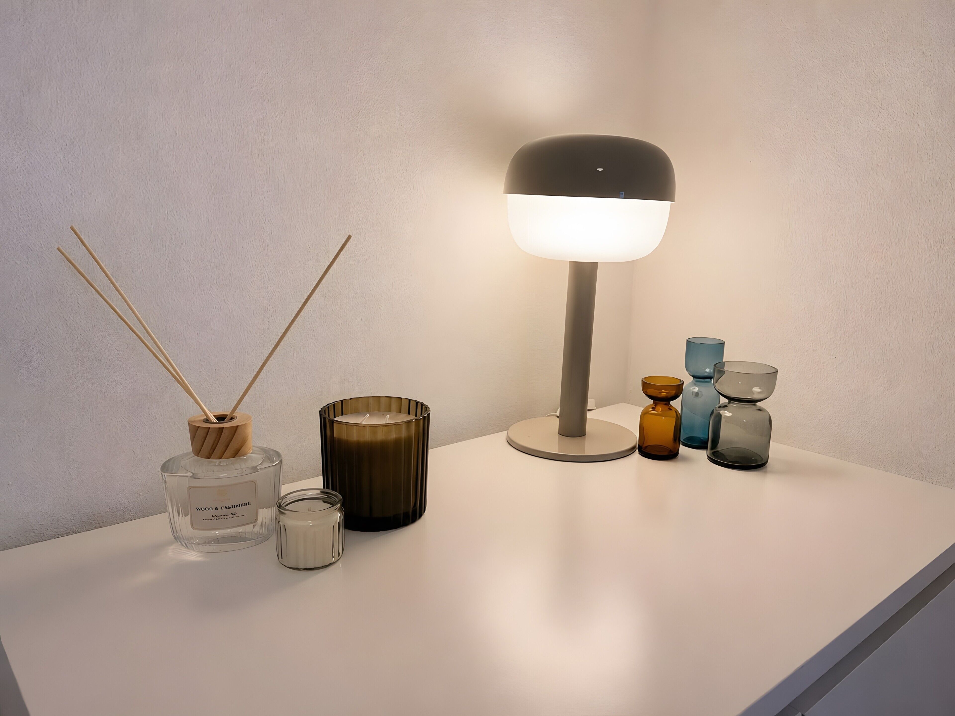 A table with a lamp, candles, and decorative jars.