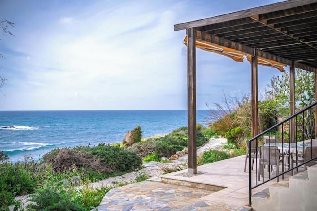 A coastal property with a stone patio, outdoor seating, and a pergola overlooking the ocean.