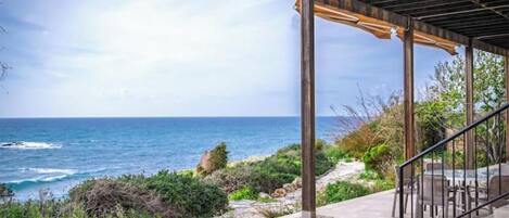 A coastal property with a stone patio, outdoor seating, and a pergola overlooking the ocean.
