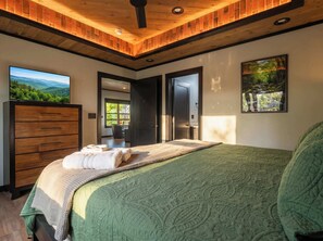 Ein Schlafzimmer mit einem Bett, einer Holzkommode, einem Fernseher und einem Gemälde.