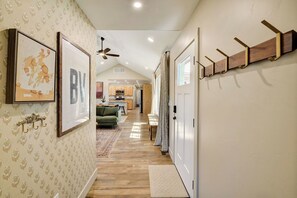 A hallway with patterned wallpaper, a ceiling fan, a coat rack, and a view into a kitchen area. - Brand New Cozy Getaway - Mountain Views + Firepit (Buena Vista)