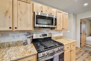 Una cocina con armarios de madera, un microondas de acero inoxidable y una estufa a gas.