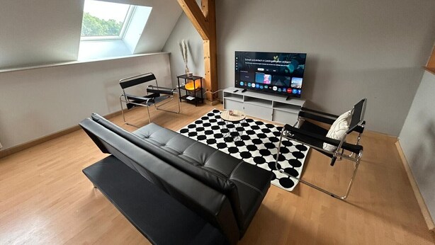 Ein modernes Wohnzimmer mit einer schwarzen Ledersofa, einem schwarz-weißen Schachbrettteppich, einem Fernseher und einem Holzbalken an der Decke.
