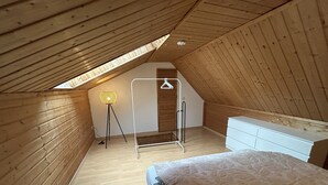 Ein kleines Schlafzimmer unter dem Dach mit niedrigem Giebeldach, einem Bett, einer Kommode und einer Kleiderstange.