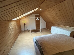 A small, sloped-roofed attic bedroom with a bed, dresser, and a hanging clothes rack. - Apartment "City Loft at Schillerpark" with Wi-Fi (Dessau-Roßlau)