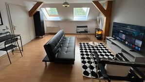 Ein modernes Wohnzimmer mit einer Couch, einem Esstisch, einem Fernseher und einem schwarz-weißen Teppich mit Muster.