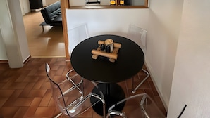 Ein Essbereich mit einem runden Tisch, Stühlen, einer Pendelleuchte und Blick auf ein Wohnzimmer mit einer Couch und einem Fenster.