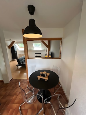 En matplats med ett runt bord, stolar, en hänglampa och utsikt över ett vardagsrum med en soffa och ett fönster.