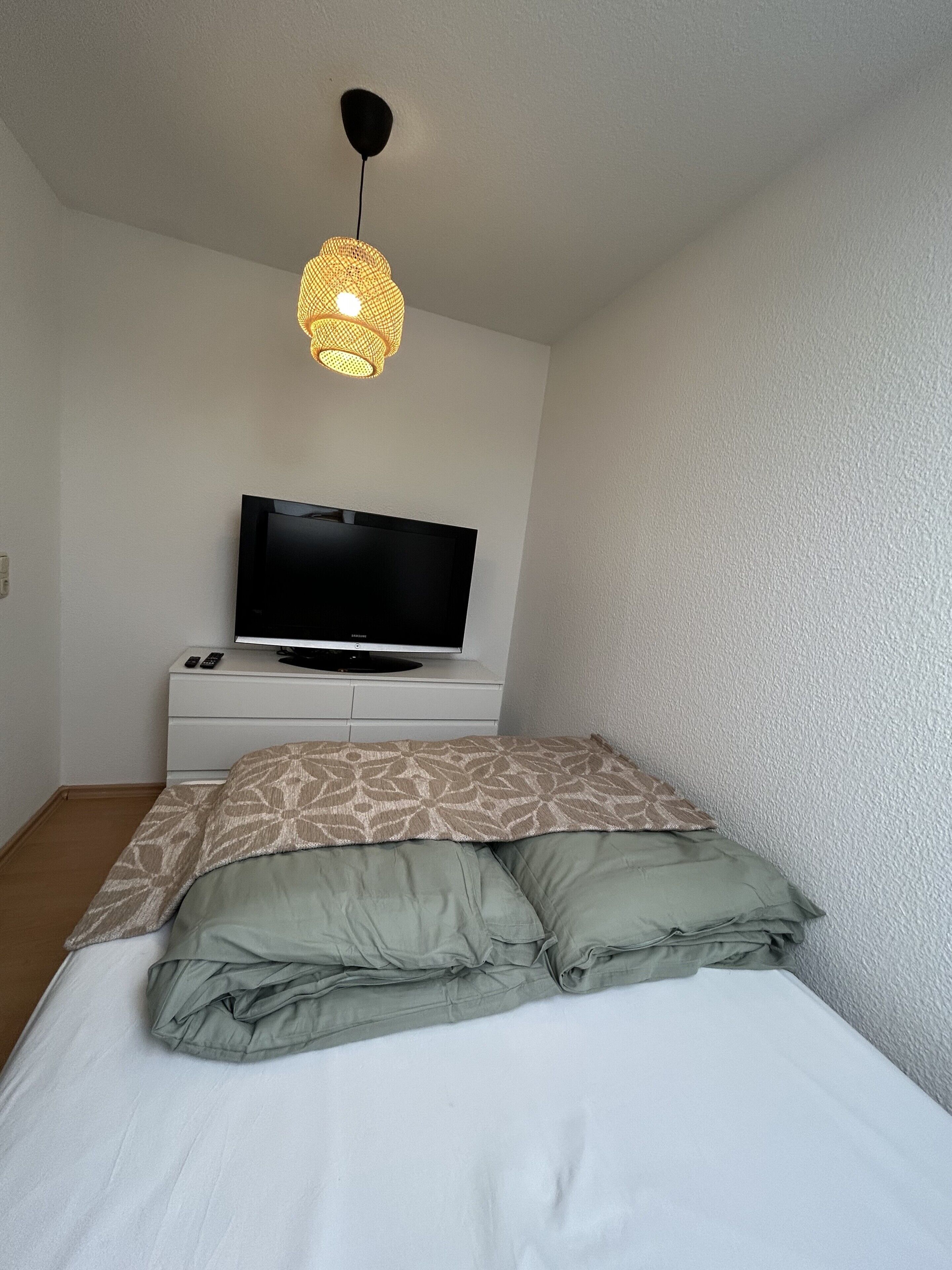 Ein Schlafzimmer mit einem Bett, einem Fernseher auf einem Schrank und einer Hängeleuchte.