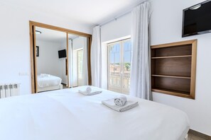 A hotel room with a large bed, a television mounted on the wall, and a balcony with a view. - #397 Comfortable Apartment by the Beach (Albufeira)
