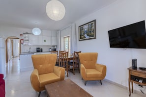 A living room with a TV, two armchairs, a wooden coffee table, and a dining area with a table and chairs. - #397 Comfortable Apartment by the Beach (Albufeira)
