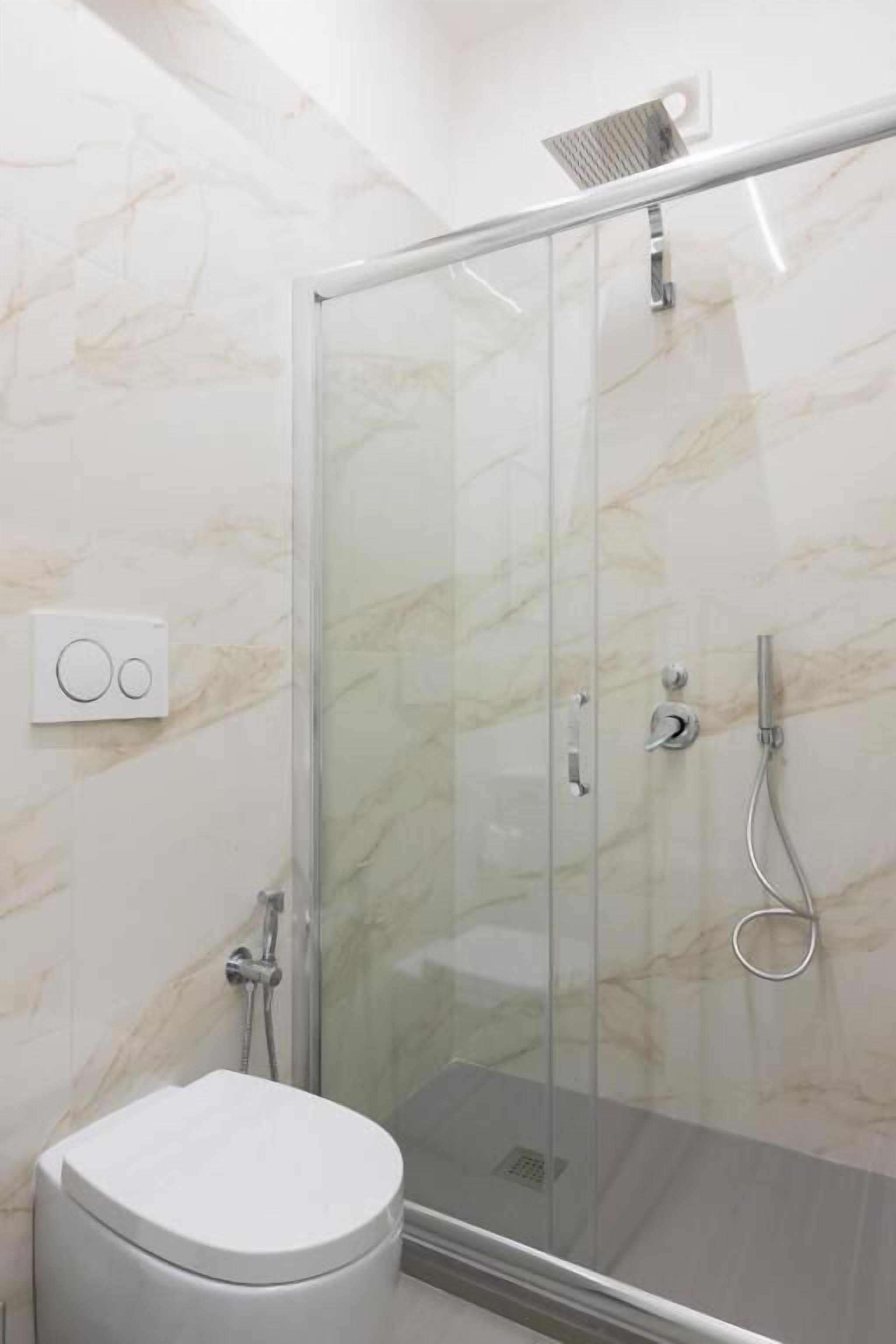 Un baño con cabina de ducha de vidrio, inodoro y pared de mármol.