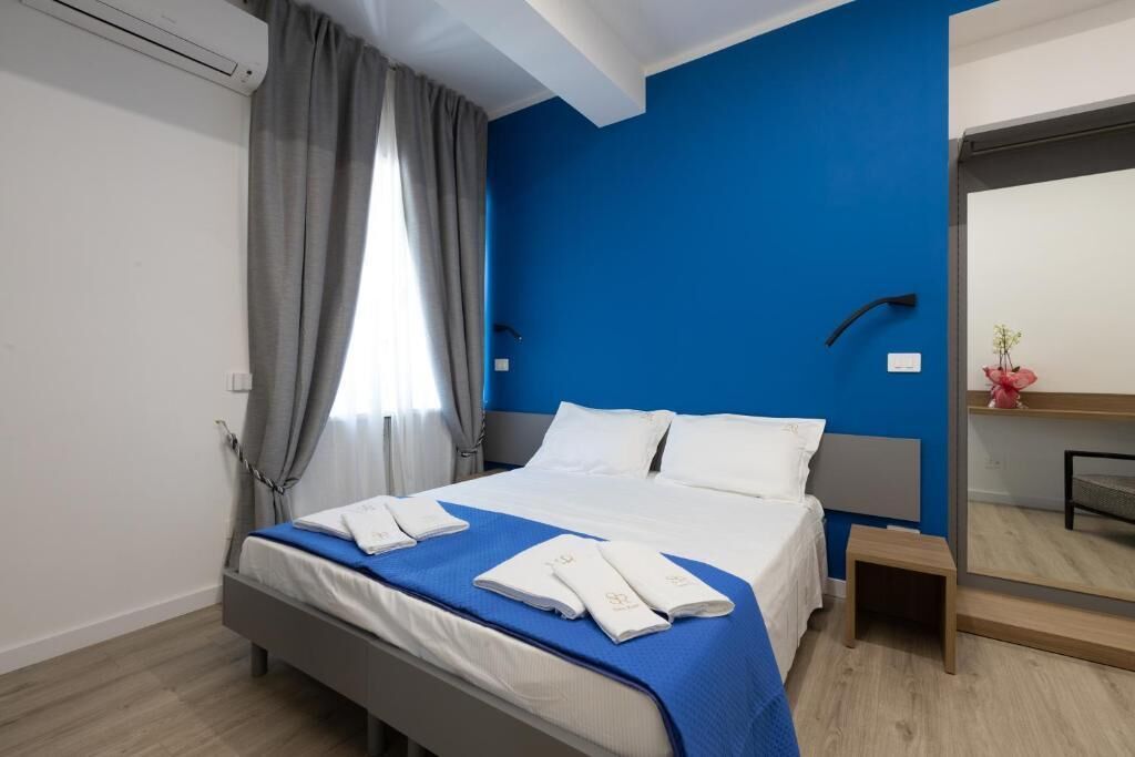 Ein Hotelzimmer mit Bett, Nachttisch, Spiegel und einem Fenster mit Vorhängen.